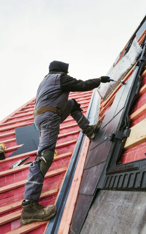 A roofer replacing the tiles on a house roof.